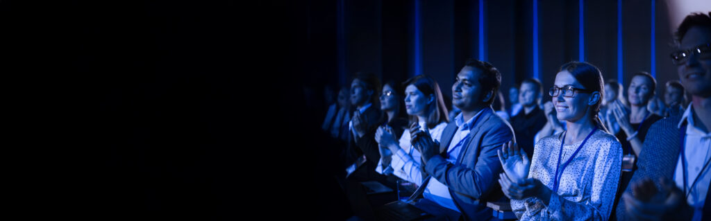 Young Woman Sitting in a Crowded Audience at a Business Conference. Female Attendee Cheering and Clapping After a Motivational Keynote Speech. Auditorium with Young Successful Businesspeople.