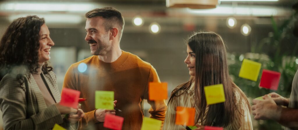 Colleagues collaborating on ideas, actively brainstorming using colorful sticky notes on a glass board in an office environment